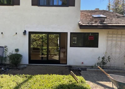 Exterior view of a two-story house with large glass sliding doors, a small garden, and a "MILDARD" sign in the window.